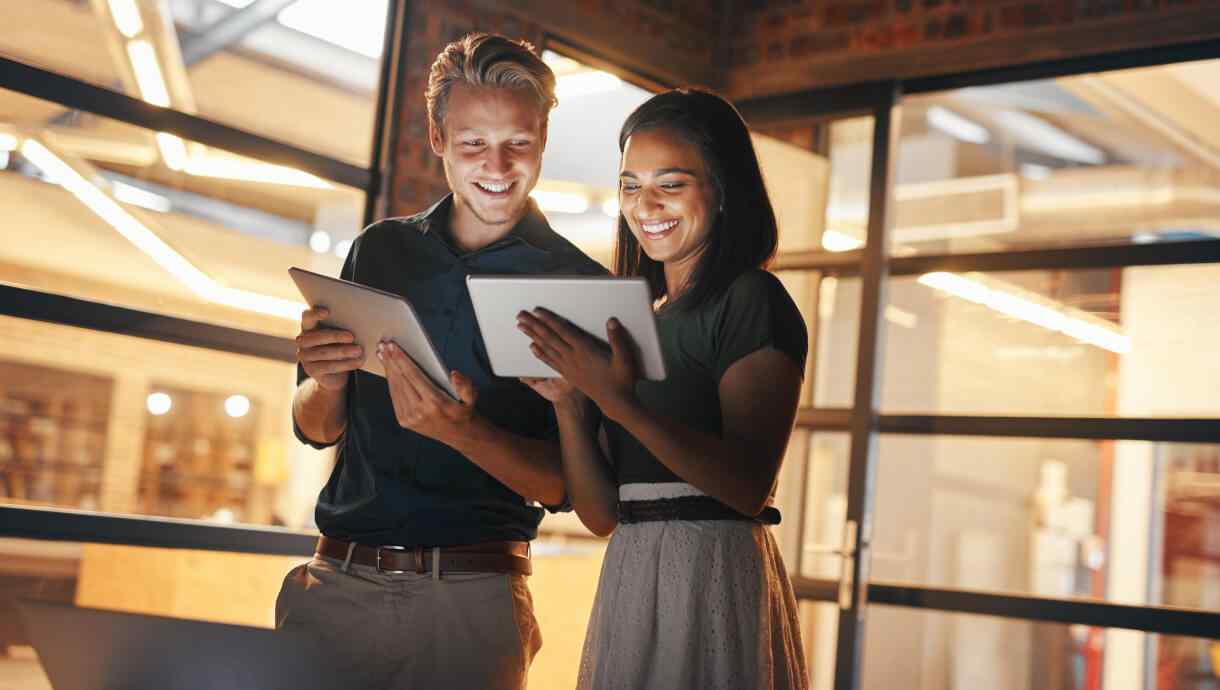 Two colleagues smiling as they look at tablets
