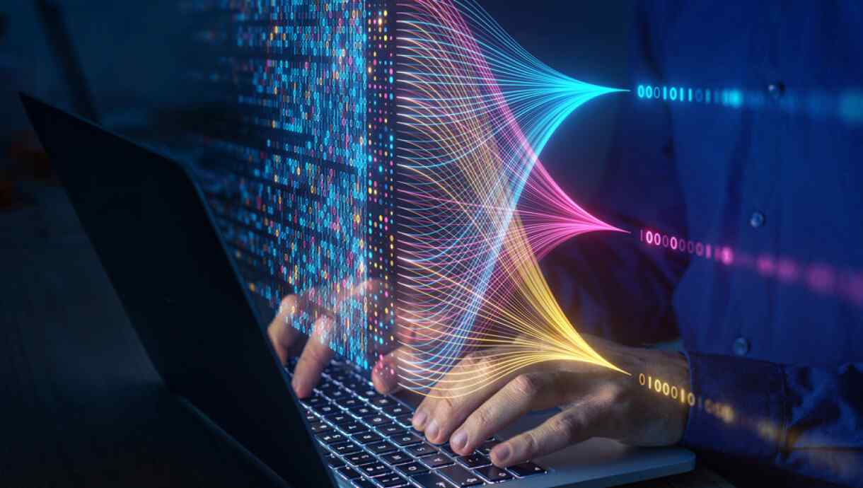 Hands typing on a laptop surrounded by streams of data